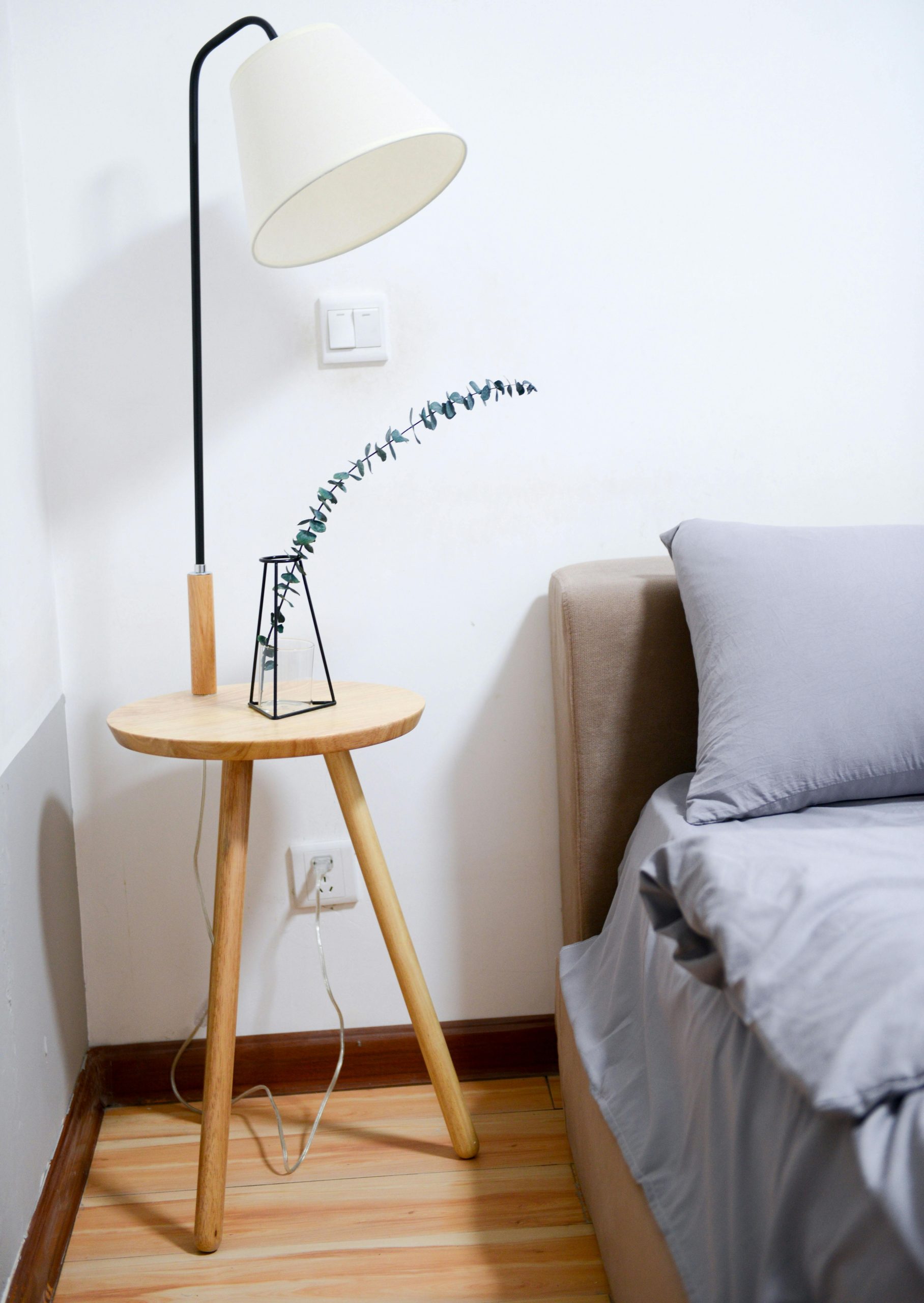 Modern minimalist bedroom with wooden nightstand, sleek lamp, and gray bedding set.